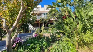 Un edificio residencial con balcones, rodeado de abundante vegetación y plantas con flores.