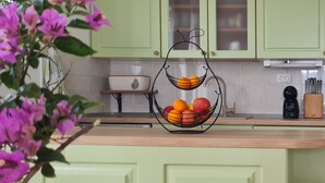 Una cocina con armarios verdes, una cesta de frutas en la encimera y una cafetera.
