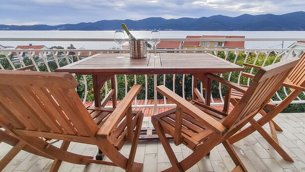 Una mesa de madera con sillas en una terraza con vistas al agua y montañas.