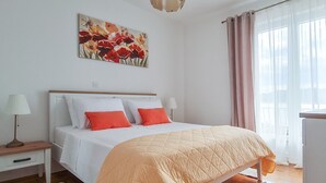 Un dormitorio con cama, mesitas de noche, lámpara, un cuadro y ventana con cortinas.