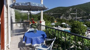 Ein Balkon mit Tisch und Stühlen, einer blauen Tischdecke, einer Blumenvase und Blick auf eine gebirgige Landschaft.