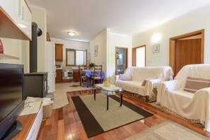 Sala de estar con televisor, sofá y mesa de centro. Se ve una cocina al fondo con una mesa de comedor y sillas.