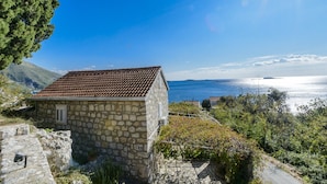 A stone building with a tiled roof, surrounded by greenery and overlooking a body of water. - Villa Soline - Two Bedroom Apartment with Terrace and Sea View (Mlini)