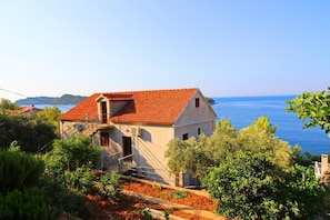 Une maison située sur la côte, avec un toit recouvert de tuiles rouges, un petit escalier et un jardin où poussent différentes espèces de plantes.