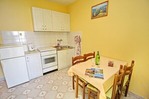 Une cuisine compacte avec des meubles blancs, un évier et une table à manger pour deux personnes, accompagnée de chaises.