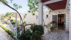 Un espacio al aire libre cubierto con suelo de piedra, plantas en macetas y una escalera metálica que conduce a la entrada de un edificio.