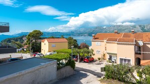 Un quartier résidentiel situé sur la côte, avec des immeubles, des voitures garées et une vue dégagée sur la mer et les montagnes en arrière-plan.