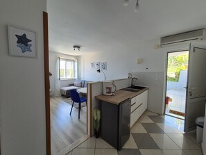 Modern kitchen with central island, sink, and refrigerator, adjacent to a dining area with a table and chair.