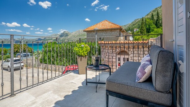 Ein Balkon mit Meerblick, ein Steinhaus und geparkte Autos.