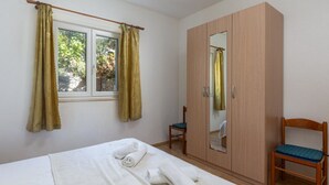 Um quarto com uma cama, um guarda-roupa, uma cadeira e uma janela com cortinas.