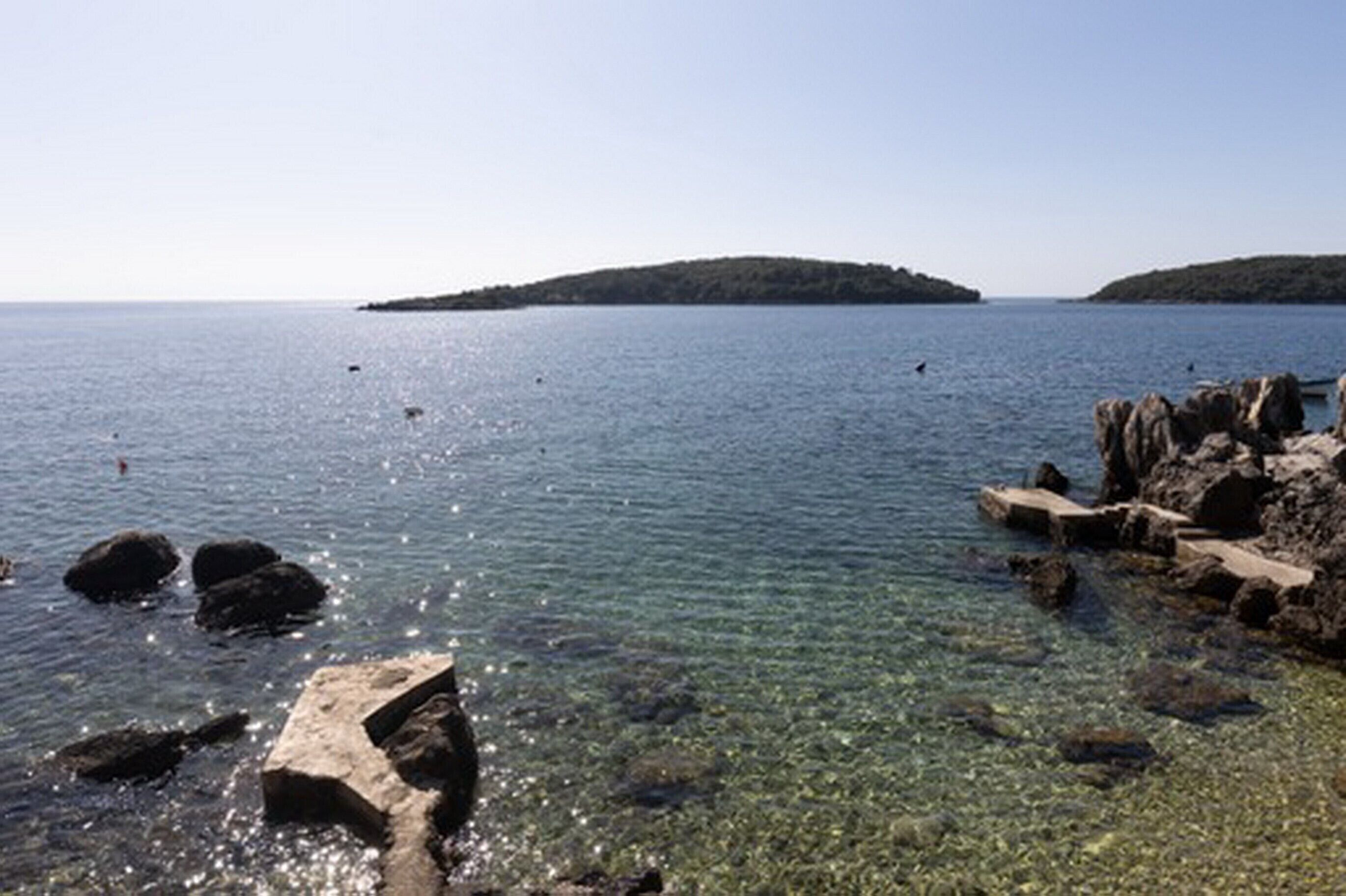 Un paysage côtier avec une eau claire, une rive rocheuse et une île au loin.