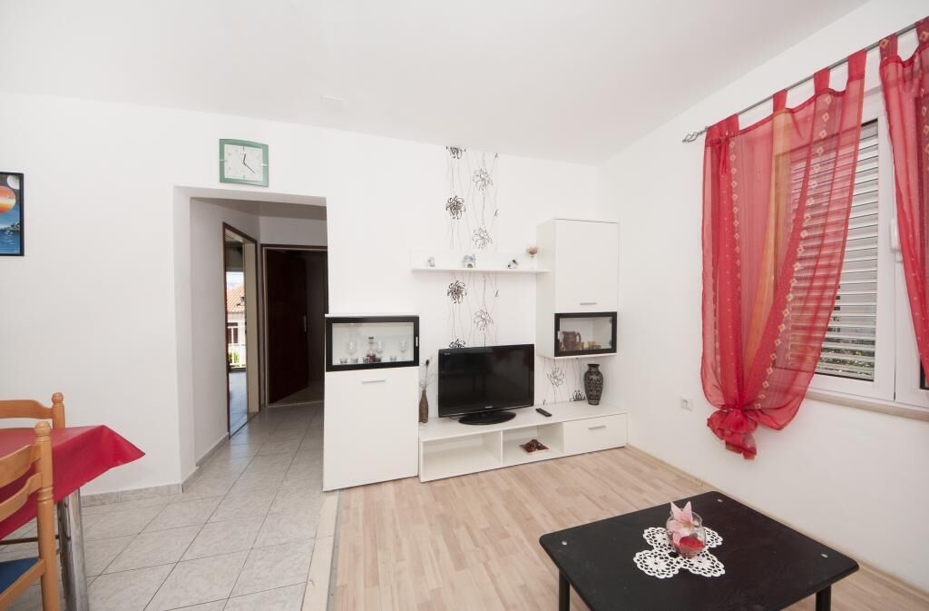 A modern living room with a TV, white cabinets, a small table, and a red curtain.