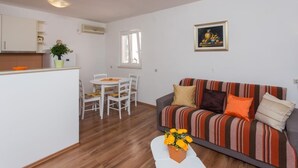 Un espace de vie compact comprenant un coin cuisine, un coin repas et un canapé agrémenté d’un coussin à rayures.