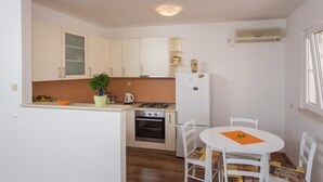 Une cuisine compacte avec des meubles blancs, une cuisinière et un réfrigérateur. On y trouve une petite table à manger avec des chaises.