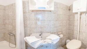 Un baño con lavamanos, inodoro, ducha y perchero para toallas.