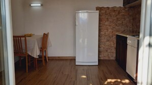 A compact kitchen with a white refrigerator, wooden dining table, and chairs. A stone wall and wooden cabinets are visible. - Guest House Oreb - Comfort Double Room (Kolocep)