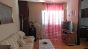Una sala de estar con sofá, mesa de centro, televisor y puerta corredera con cortinas.