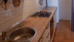 Una cocina con armarios blancos, un lavamanos de acero inoxidable, una estufa a gas y un microondas.