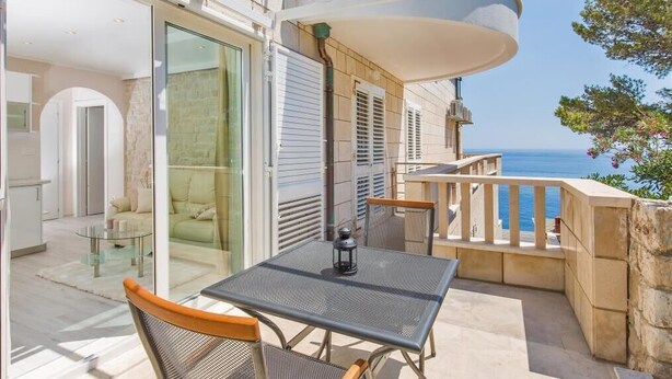 A balcony with a table and chairs, a view of the sea, and a glass door leading to an interior space.
