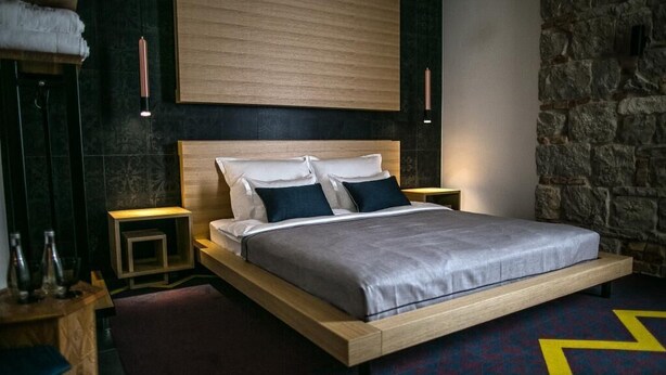 A modern bedroom with a wooden bed, two bedside tables, a stone wall, and a patterned carpet. - Rooms Lejletul  - Deluxe Double Room with Square View (Berat) (Split)