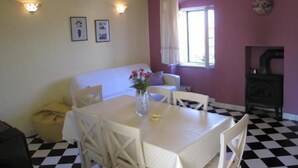 A dining area with a checkered floor, a white table with chairs, a vase with flowers, a sofa, and a fireplace. - Apartment Glavica- Two Bedroom Apartment with Terrace (Supetar)