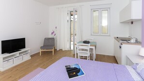 A modern, well-lit room with a bed, a TV, a desk, and a kitchenette. - Apartments Villa Karmen - Studio with Terrace (Lavanda) (Dubrovnik)