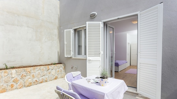 An outdoor seating area with a table and chairs, a potted plant, and a door leading to an interior room. - Apartments Villa Karmen - Studio with Terrace (Lavanda) (Dubrovnik)