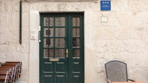 Eine grüne Tür mit Fenster, ein Schild darüber und ein Stuhl zur rechten Seite.