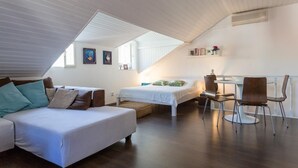 Ein modernes Schlafzimmer im Loftsstil mit schrägem Dach, zwei Betten, einem Esstisch und einem Stuhl.