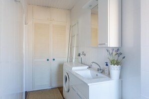 Ein kleines, modernes Badezimmer mit Waschmaschine, Waschbecken und Spiegel.