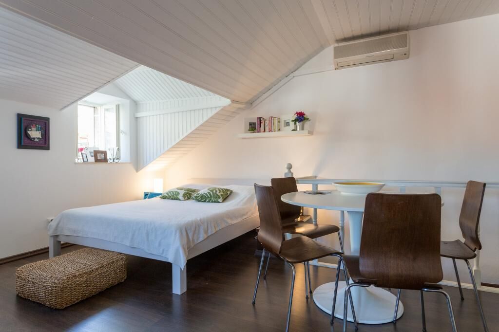 Une chambre à coucher comprenant un lit, une table de chevet, une chaise, une petite table et une étagère avec des livres et des fleurs.