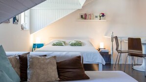 Ein Schlafzimmer mit einem Bett, Nachttischen, einem Schreibtisch und einem Stuhl. Über dem Bett befindet sich ein Oberlicht und ein Regal mit Büchern und Blumen.
