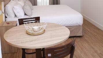 Habitación de hotel con cama, televisor montado en la pared, una mesa de comedor con sillas y una ventana con cortinas.