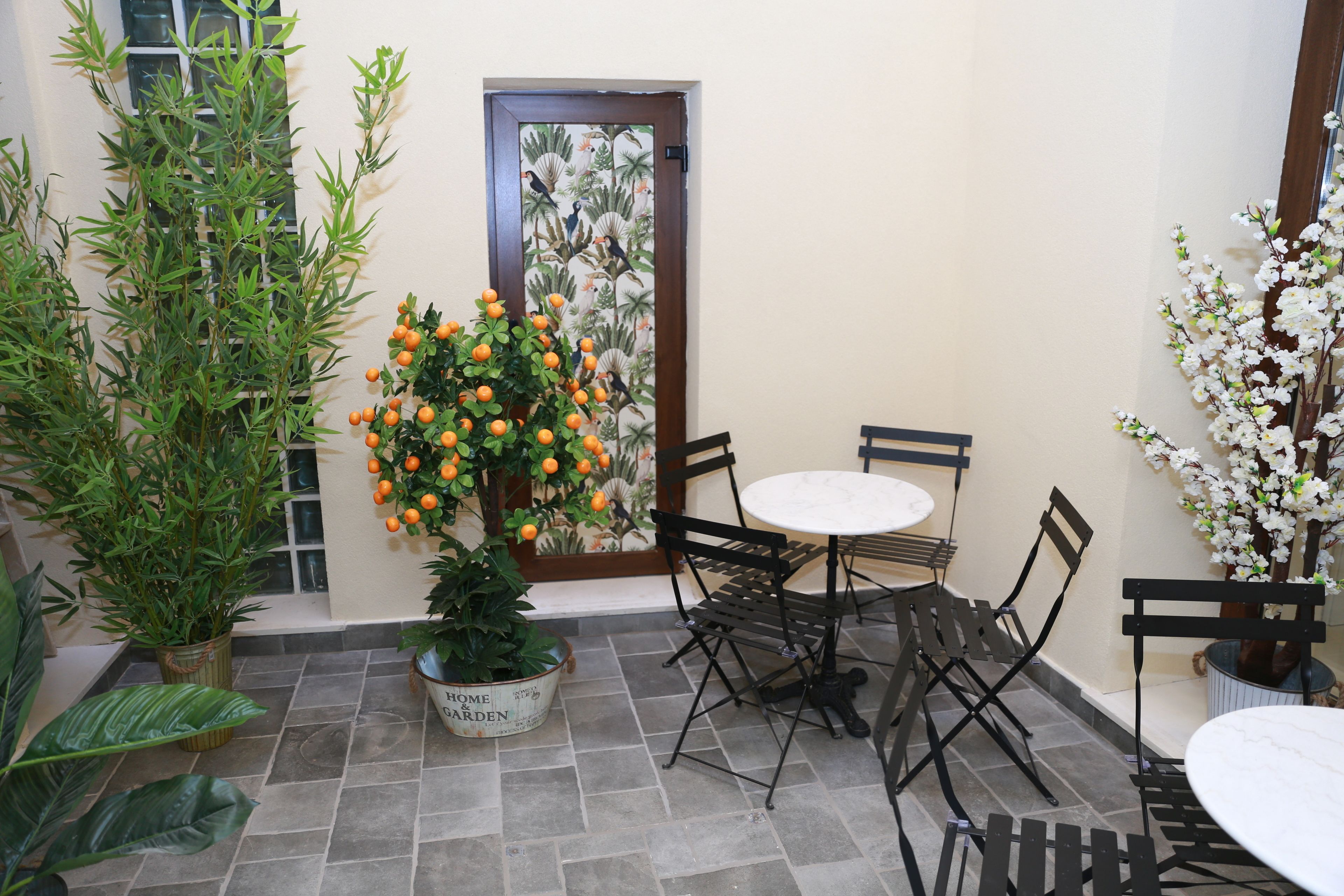 Eine Terrasse mit Tisch, Stühlen, Blumentöpfen und einer Tür mit floralem Dekor.