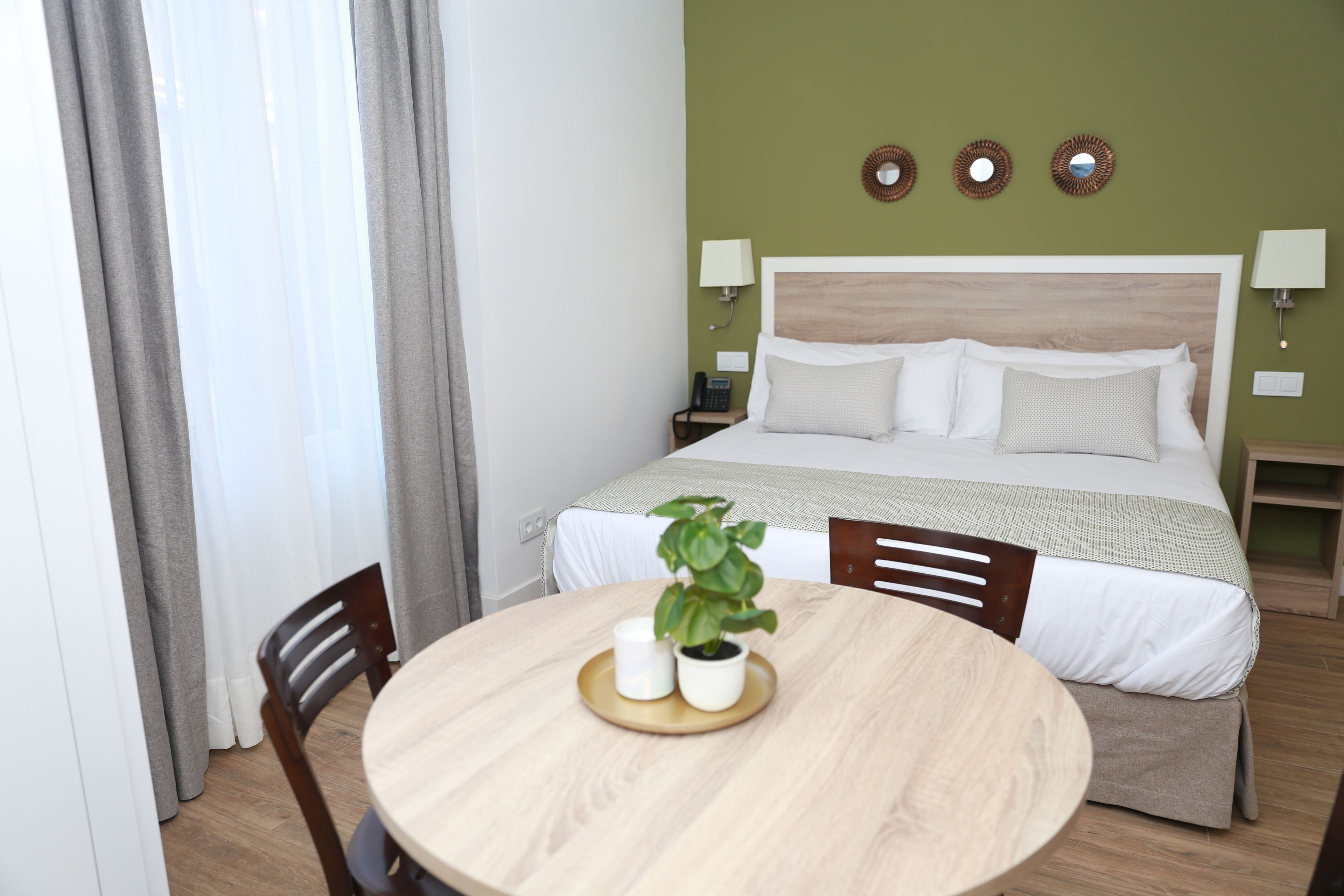 A hotel room with a bed, bedside tables, a round wooden table with a plant, and a chair.