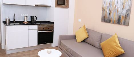 A compact living space with a kitchenette, a sofa with cushions, and a small table.