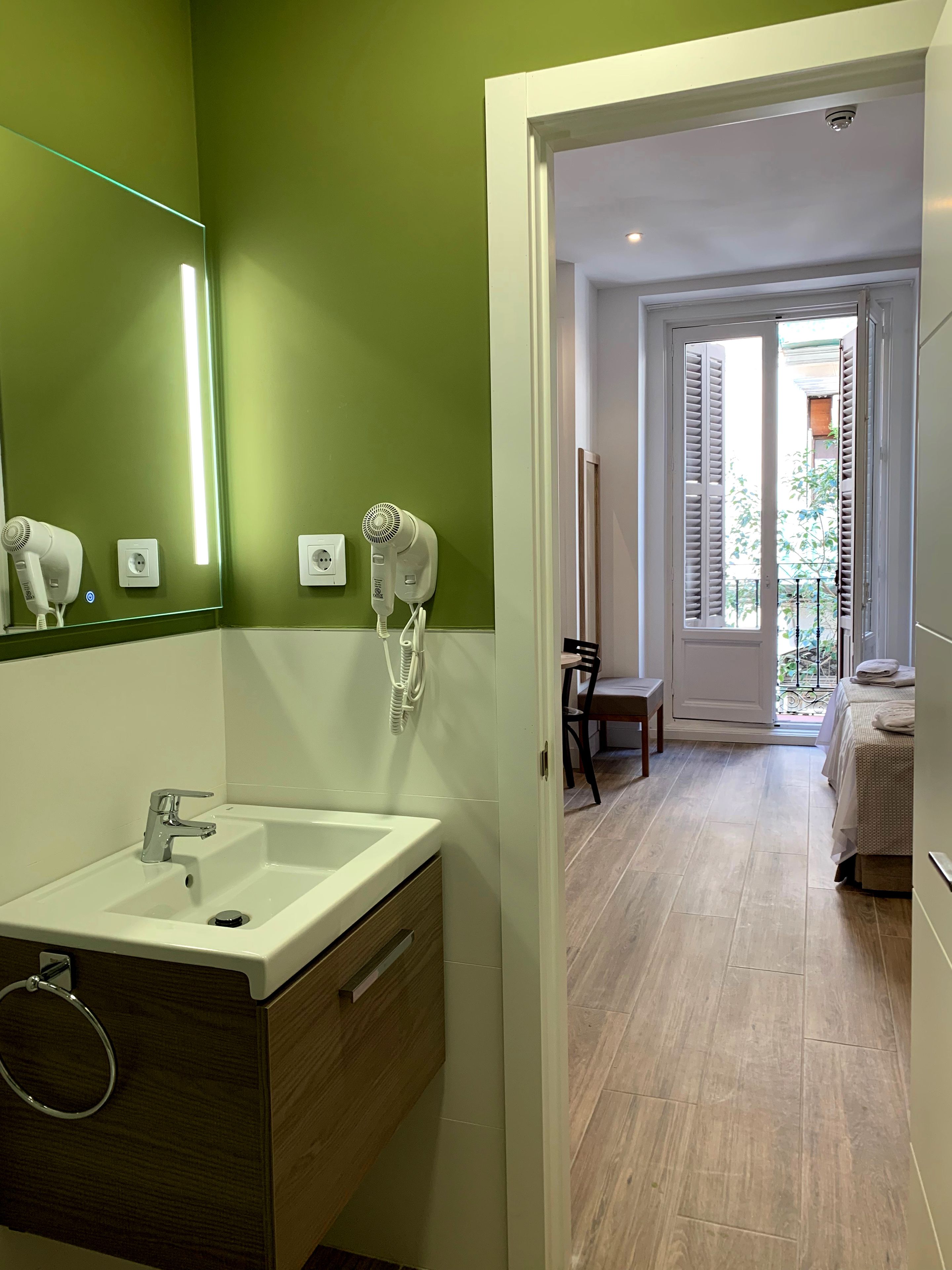 Un bagno moderno con una parete verde, un lavandino bianco e due asciugacapelli fissati al muro.