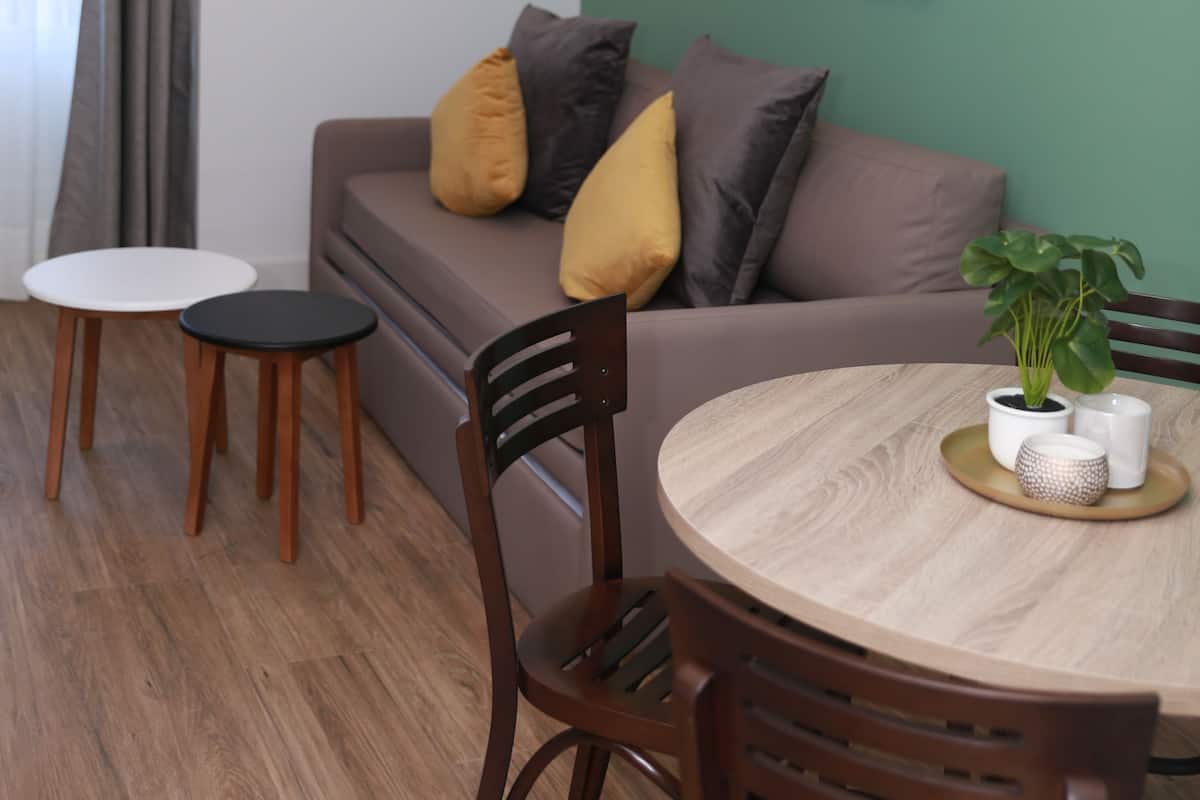 Un salon moderne avec un canapé, deux petites tables, une table à manger en bois et un mur d’accent vert.