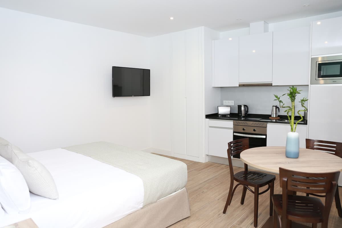 Une chambre d’hôtel moderne équipée d’un lit, d’une table à manger avec des chaises, d’un coin cuisine avec un four à micro-ondes et d’un téléviseur fixé au mur.