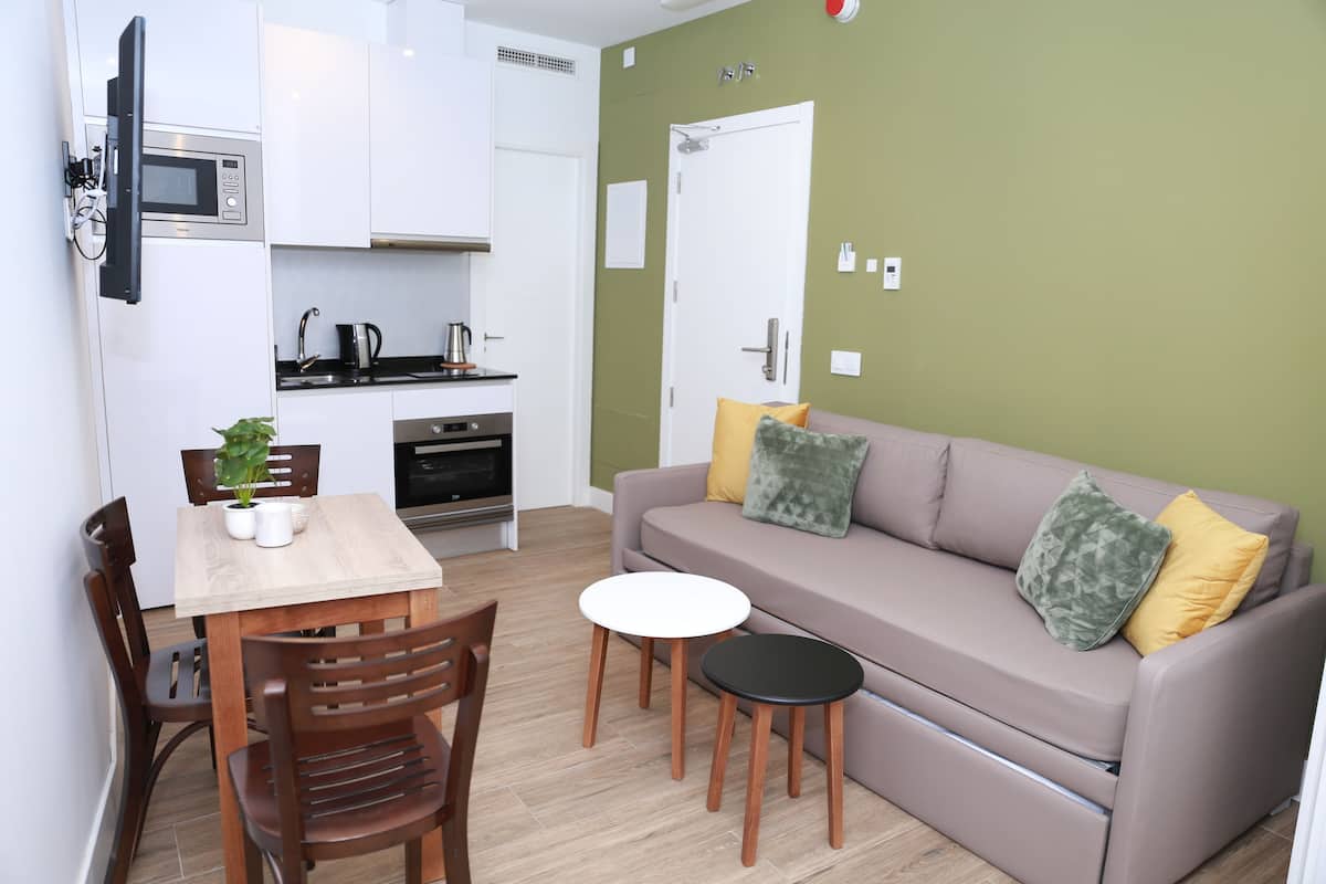 Un espace de vie compact comprenant un coin cuisine, un canapé avec des coussins, une table à manger avec des chaises et une petite table d’appoint.