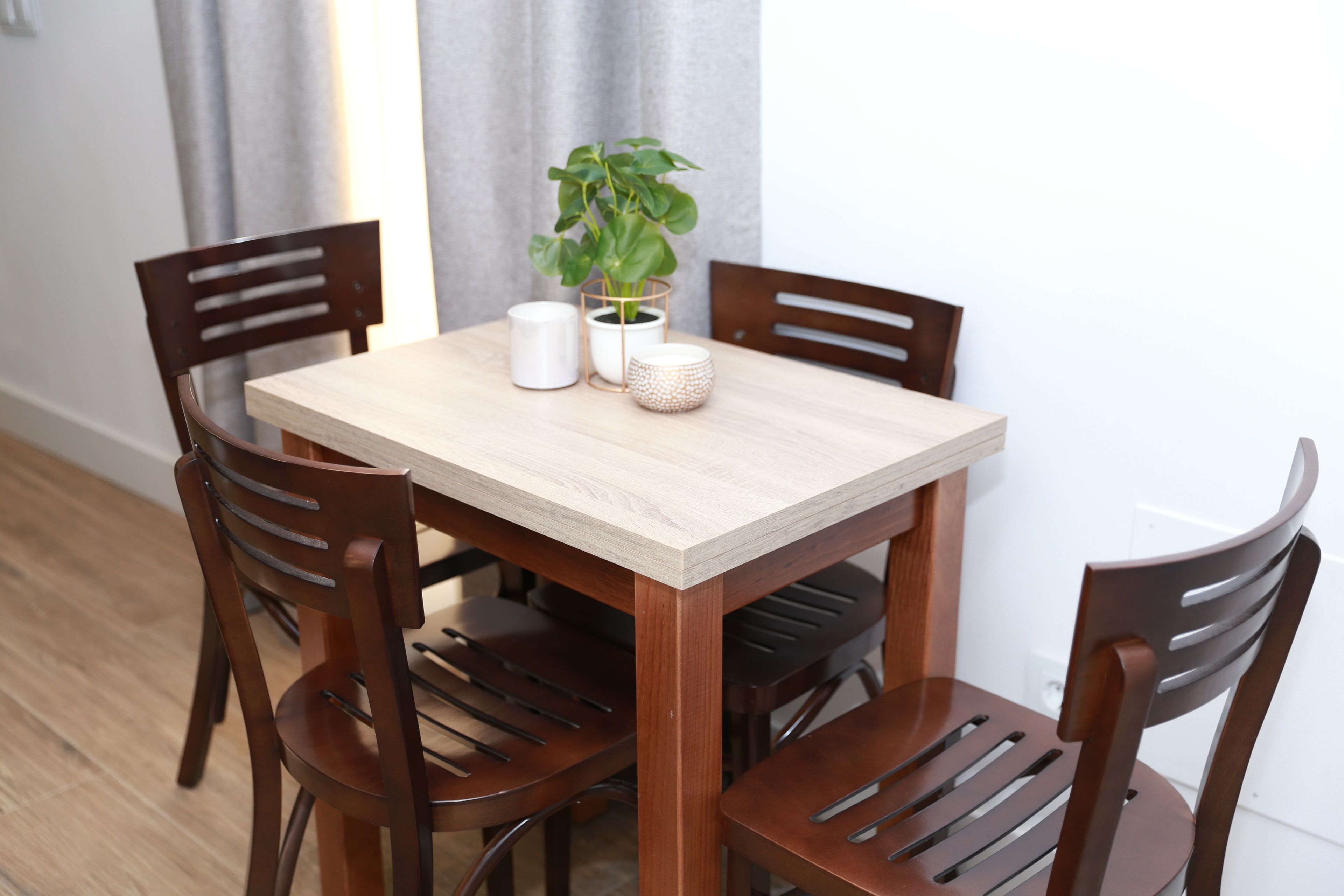 A dining table with four wooden chairs, a potted plant, and two white ceramic containers.