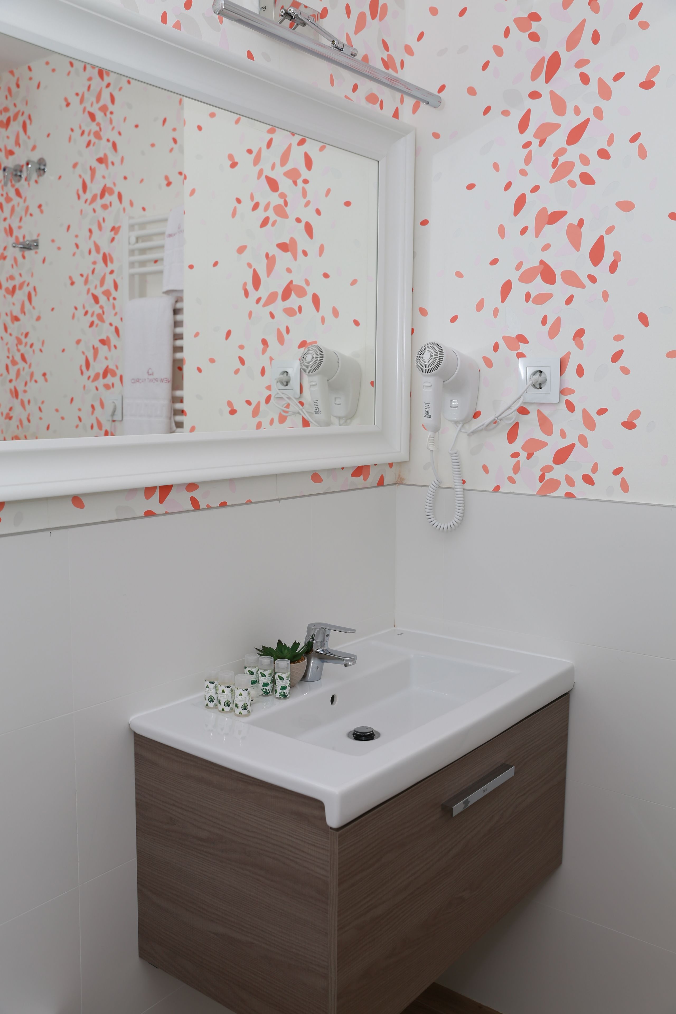 A bathroom with a white sink, a mirror, and a hairdryer mounted on the wall.