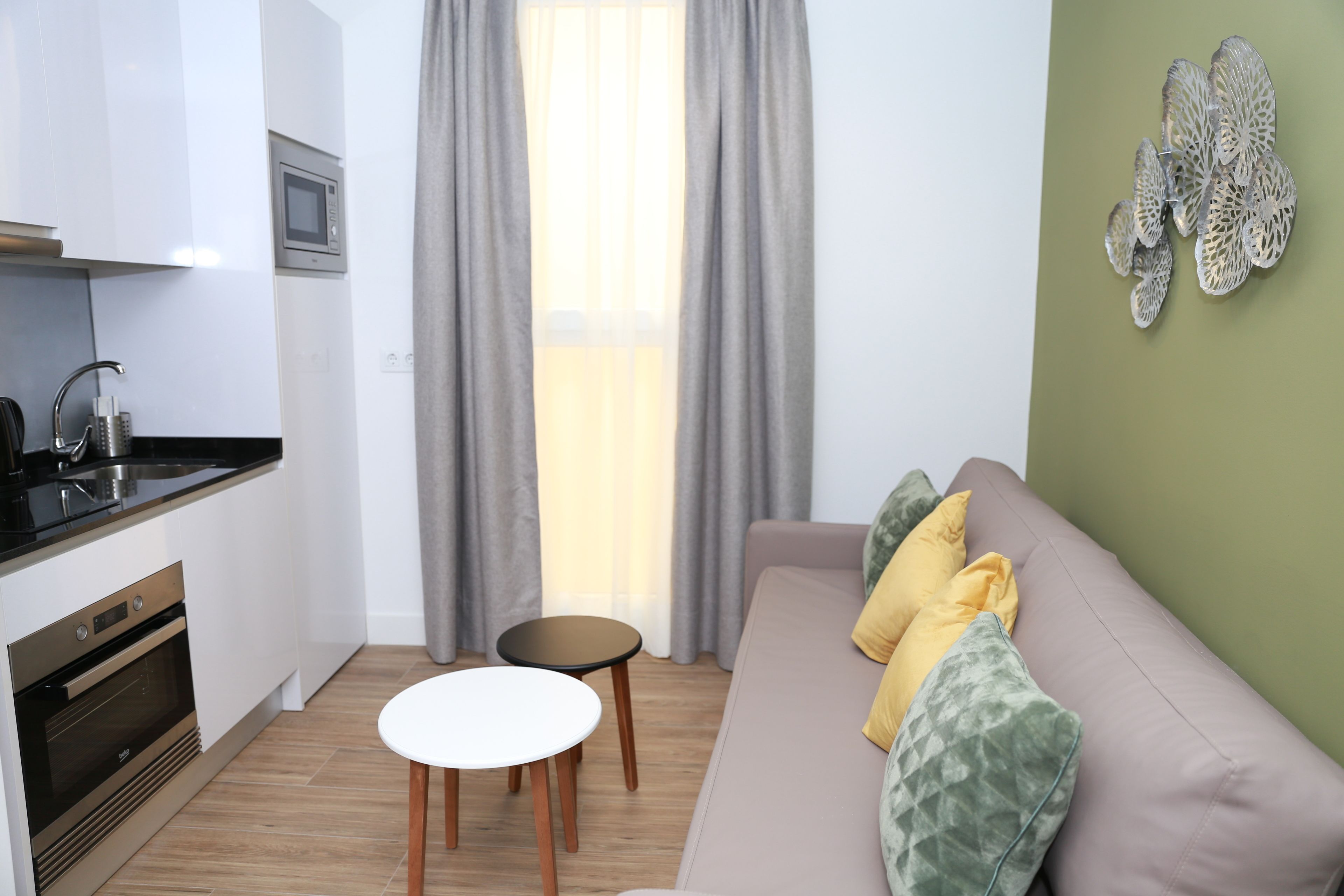 A compact living space with a kitchenette, a sofa with cushions, a small round table, and a decorative wall piece.