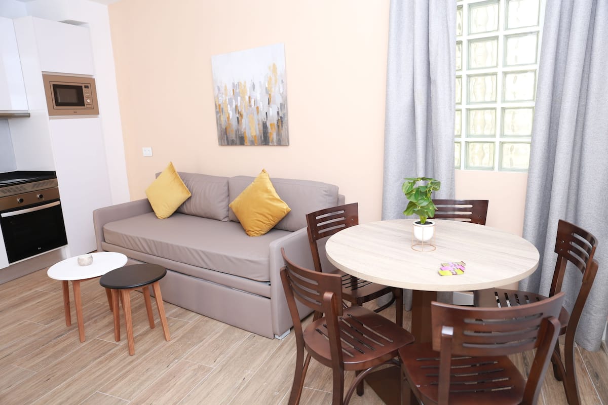 Un salon moderne avec un canapé, deux petites tables et une table à manger avec des chaises.