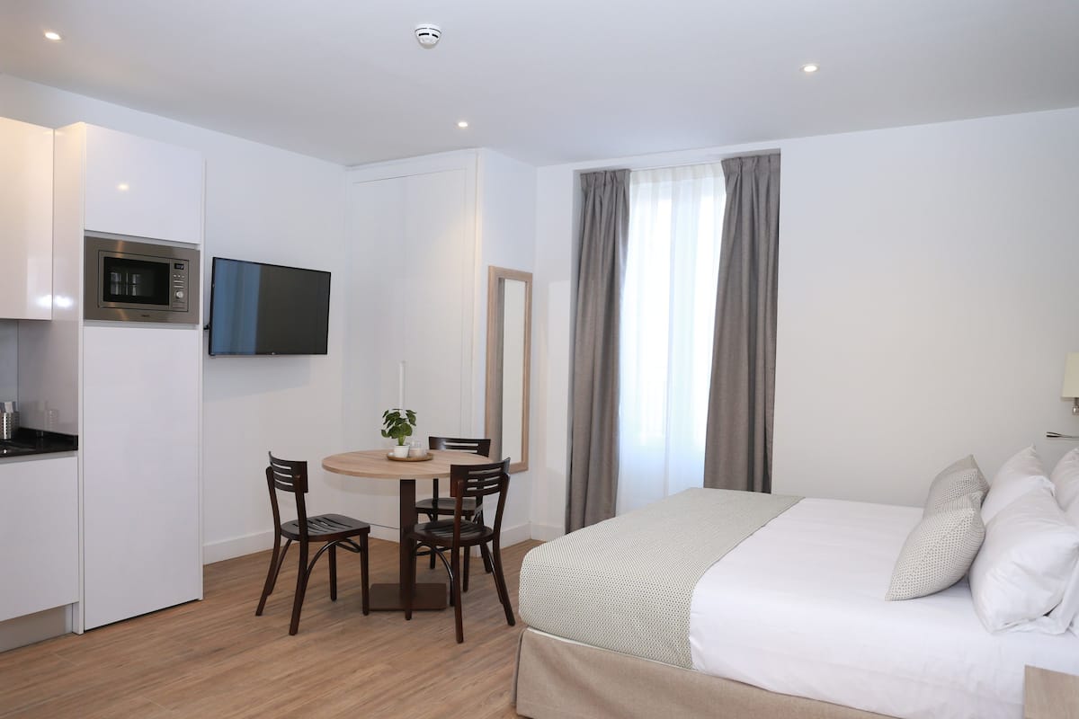 Une chambre d’hôtel compacte comprenant un lit, une petite table à manger avec des chaises, un four à micro-ondes et un téléviseur fixé au mur.