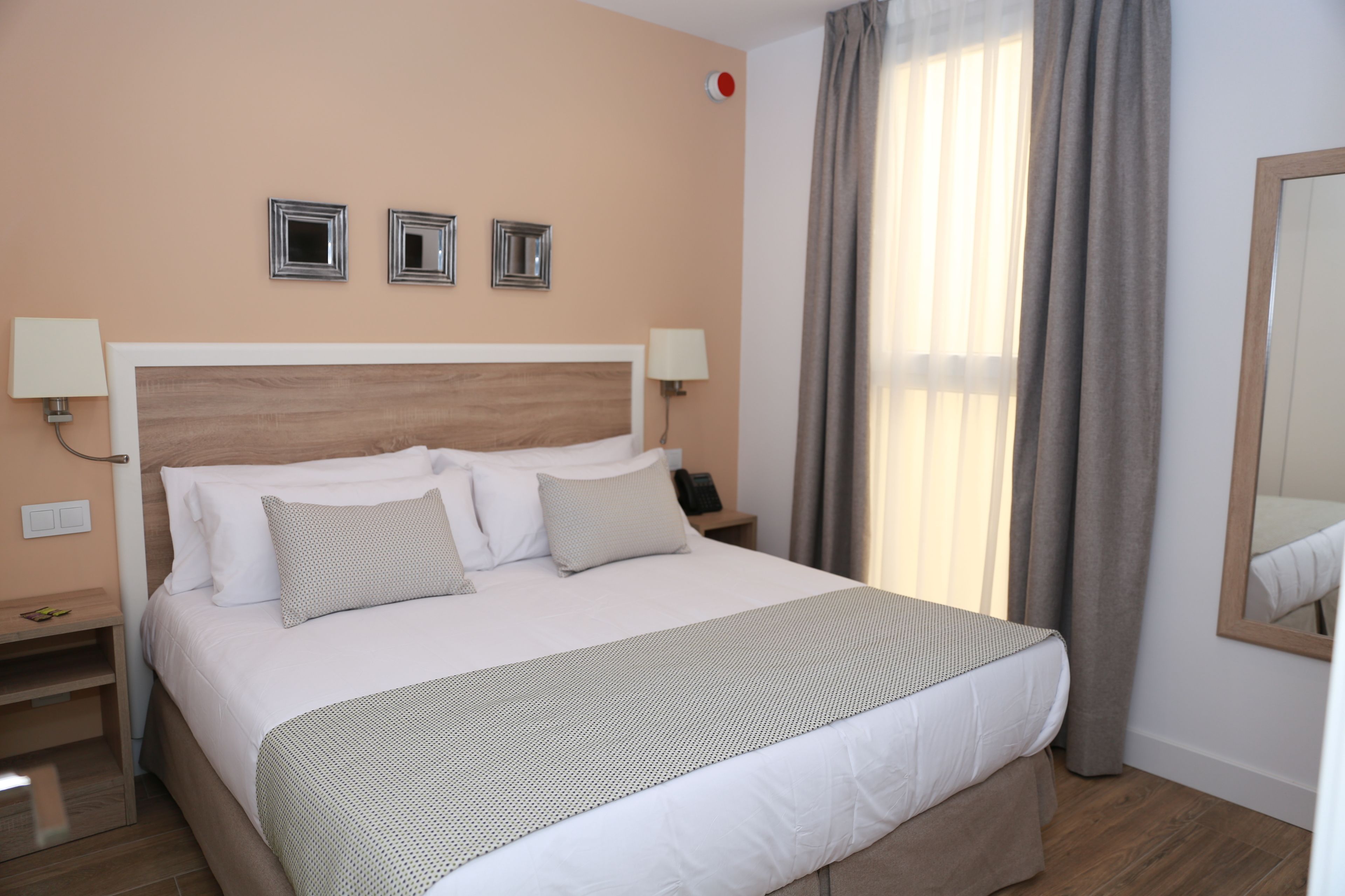 Habitación de hotel con una cama grande, dos mesitas de noche, un tocador, un espejo y una ventana con cortinas.
