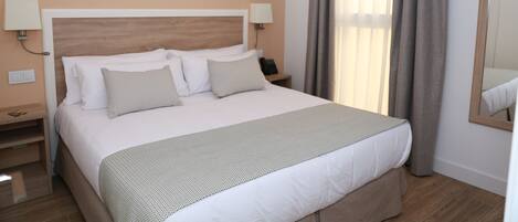 Habitación de hotel con una cama grande, dos mesitas de noche, un tocador, un espejo y una ventana con cortinas.
