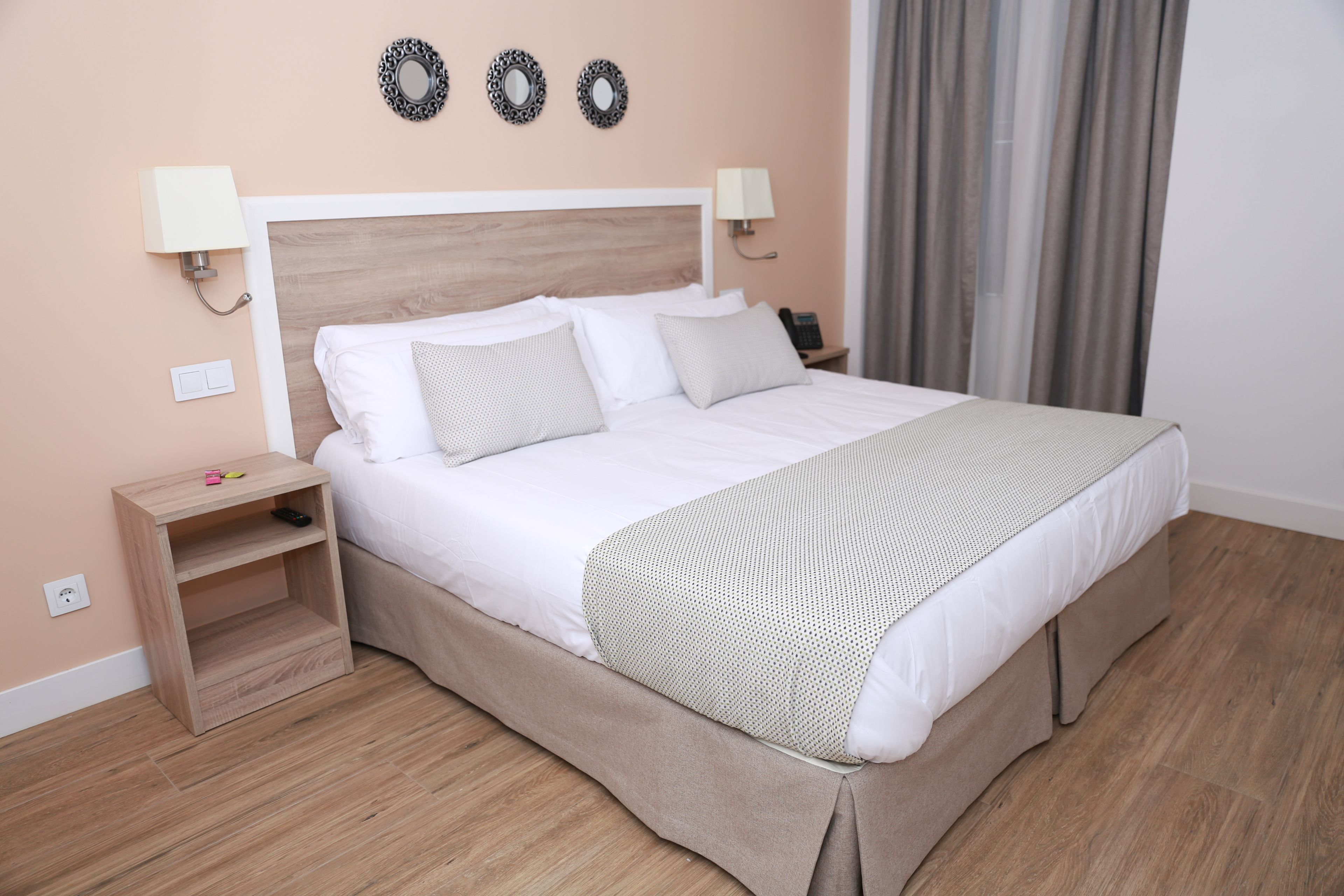 A neatly made bed with a wooden headboard, two bedside tables, and a wall-mounted lamp.