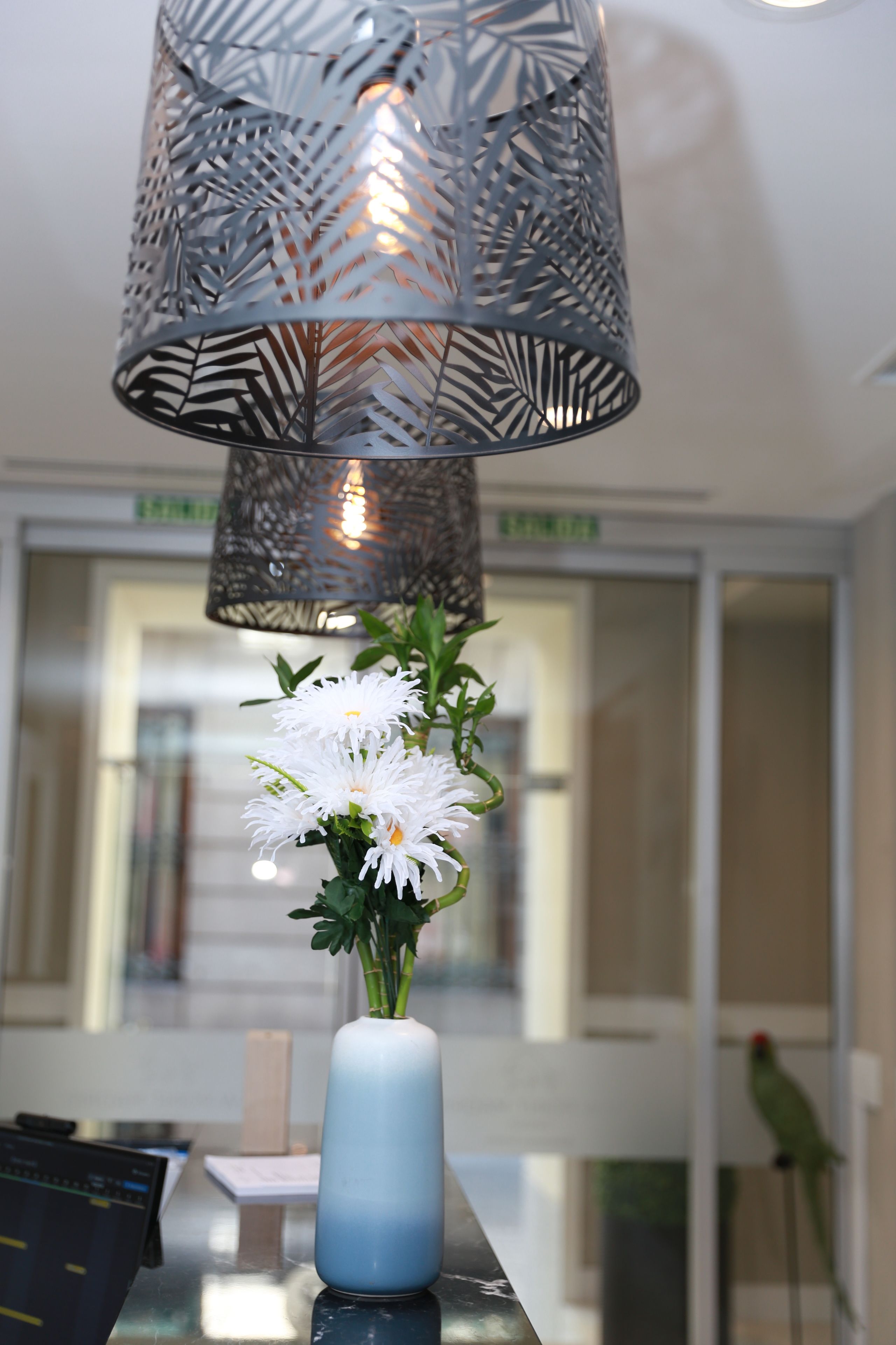 A modern interior with a decorative metal lamp, a vase with white flowers, and a bird perched on a window sill.