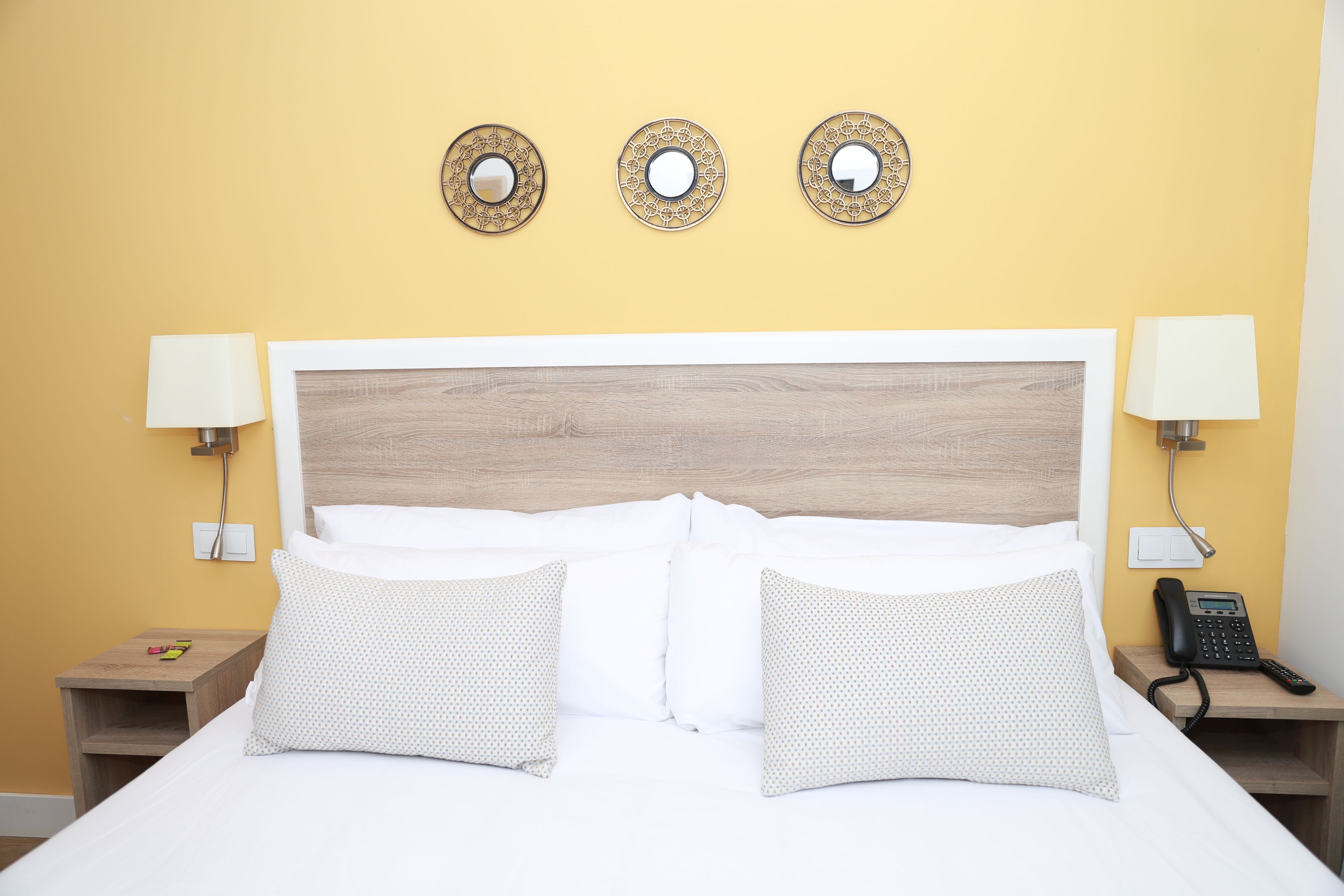 A hotel room with a large bed, two bedside tables, a wall-mounted phone, and three decorative mirrors.